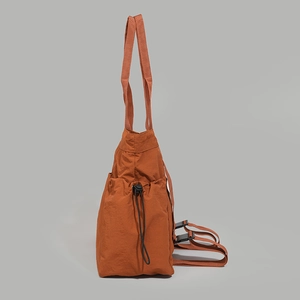 Burnt orange nylon tote bag side detail featuring adjustable drawstring pocket and strap