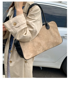 Detail of light brown suede tote bag with black leather handles held by a model