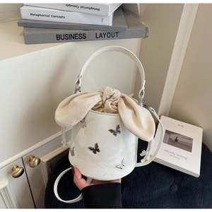 Detail of white bucket bag featuring silver metal butterfly charms and beige drawstring