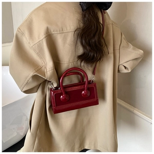 Detail of burgundy glossy patent leather mini square bag with metallic handles