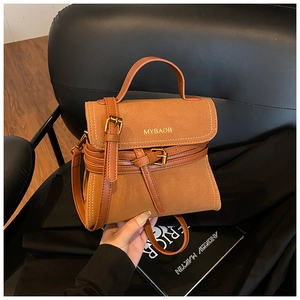 Detail of matte brown crossbody bag with gold logo on a leather chair