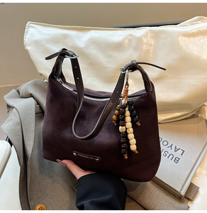 Detail of a dark brown suede dumpling bag with a bead tassel and metal brand logo