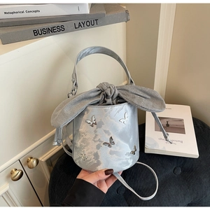 Detailed view of silver satin bucket bag with metal butterfly charms and oversized bow