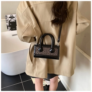 Fashionable leopard print handbag with black patent leather trim on a stylish model
