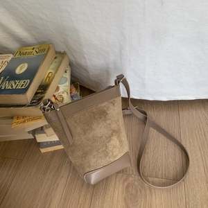 Detail of khaki suede bucket bag with leather accents on a minimalist wooden background