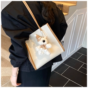 Detail of cream pebbled leather tote bag with brown trim and cute teddy bear charm
