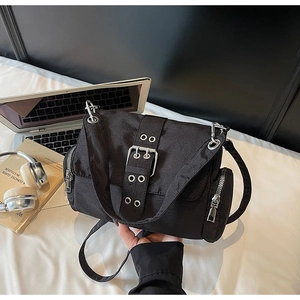 Détail du sac bandoulière en nylon noir avec boucle argentée et œillets au style techwear