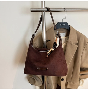 Detail of dark brown suede dumpling bag with vintage wooden beads and metal logo plate