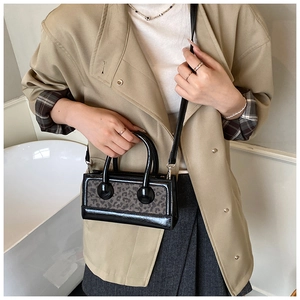 Detail view of small leopard print handbag with black patent leather trim on beige trench coat