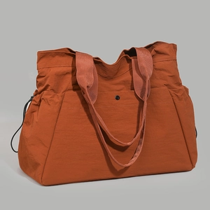 Detail view of large orange tote bag with drawstring sides and buttoned pocket