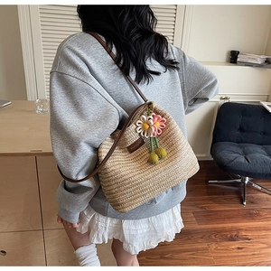Detail einer beige gewebten Beuteltasche mit Lederriemen und Häkelblumenanhänger