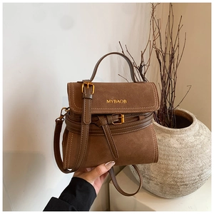 Detail of a brown suede crossbody bag with decorative buckle straps and top handle