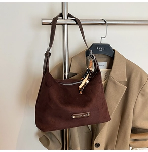 Detail of dark brown suede dumpling bag with beaded charm and metal logo on a display stand