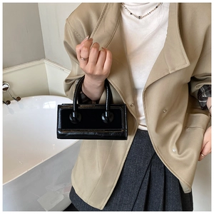 Detail view of mini black handbag with glossy and matte leather textures and spherical handle
