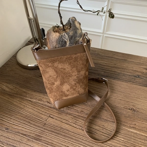 Close-up of vintage brown suede bucket bag on a rustic wood surface with warm lighting