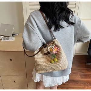 Detail der gewebten Strohtasche mit Blumenanhänger und schmalem braunem Lederriemen