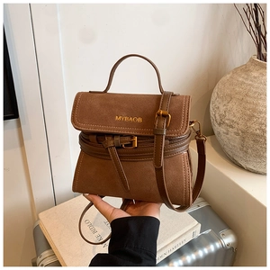 Detailed view of vintage brown suede crossbody bag with gold logo on a silver suitcase