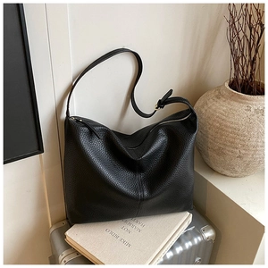 Close-up of black lychee texture leather hobo bag on a silver suitcase with art books