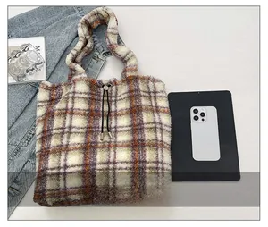 Detail view of large checkered plush tote bag showing size scale with a smartphone