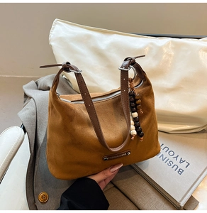 Detail of brown suede dumpling bag with leather strap and decorative wood bead charm