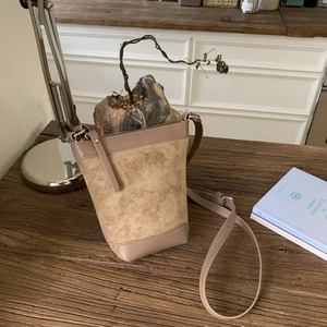 Detail of khaki bucket bag with suede texture and leather strap on a wooden table