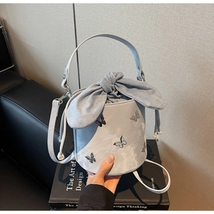 Detail of drawstring bucket bag featuring large bow and metallic butterfly ornaments