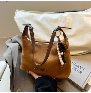 Detail of caramel suede crescent bag with dark brown strap and beaded accessory