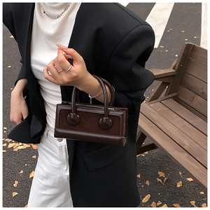 Detail of dark brown rectangular handbag with mixed leather textures in a street setting