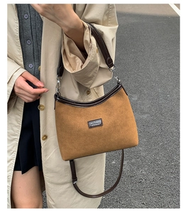 Detail of a brown suede crossbody bag with leather trim and stylish logo patch
