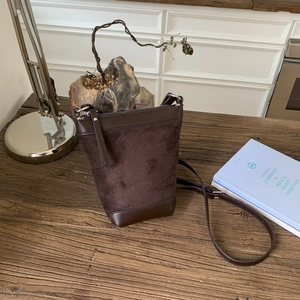 Detailed macro view of dark brown suede bucket bag with leather trim on a wooden table