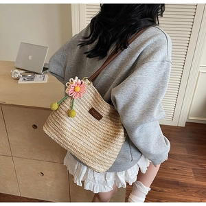 Detail der beige geflochtenen Stroh-Beuteltasche mit Lederriemen und Blumenanhänger