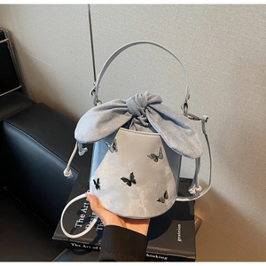 Close-up of light blue bucket bag with silver butterfly charms and fabric bow detail