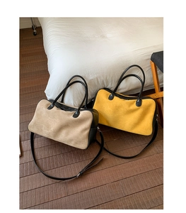 Detail of two retro suede Boston bags in khaki and yellow on a bed in a cozy home setting
