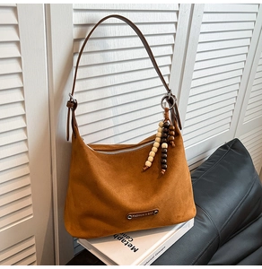 Detail of a brown faux suede hobo bag featuring a metal plate and wooden bead pendant