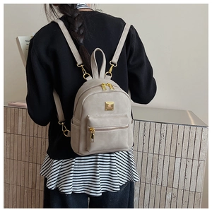 Macro detail of the beige backpack featuring gold zippers and front pocket with textured finish