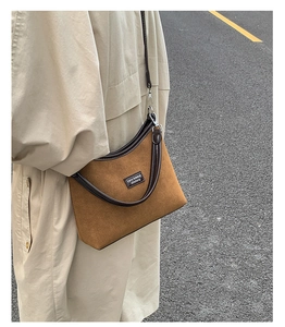 Outdoor view of a brown suede underarm bag with leather trim and shoulder strap