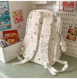 Detail of white star print school backpack with plush ball charm on a green desk