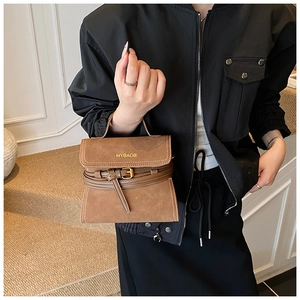 Detail of brown matte leather handbag featuring gold logo and decorative buckle strap