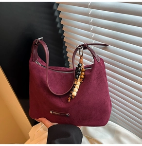 Close-up of burgundy suede hobo bag with wood bead charm and metal fashion logo tag