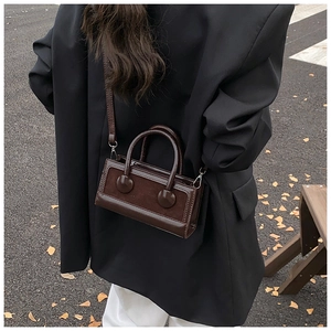 Outdoor shot of a deep brown crossbody bag with circular handles and silver hardware