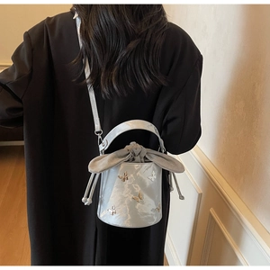 Detail of silver marble-textured bucket bag with butterfly metal accents on a model