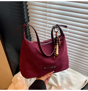 Detail of burgundy faux suede dumpling bag with bead charm and fashion logo plaque