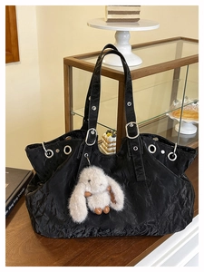 Dettaglio della borsa tote nera con occhielli argentati e ciondolo a coniglio bianco