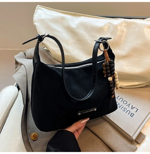Detail of black suede dumpling bag with leather strap and wooden bead charm on a blazer
