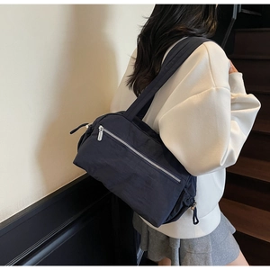 Detail view of navy blue minimalist nylon shoulder bag with silver metal zippers on model