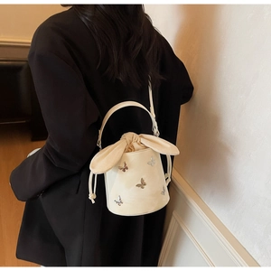 Detail of cream bucket bag featuring silver butterflies and rabbit ear drawstring closure