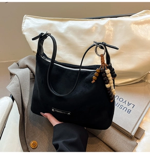 Detail of black suede dumpling bag with silver metal tag and wooden bead charm accessory