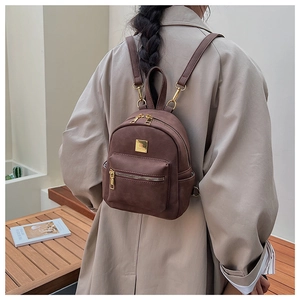 Close-up of brown suede mini backpack with golden zippers and adjustable straps on model