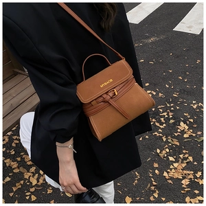 Close-up of caramel suede crossbody bag with gold MYBAOB logo in an autumn street setting