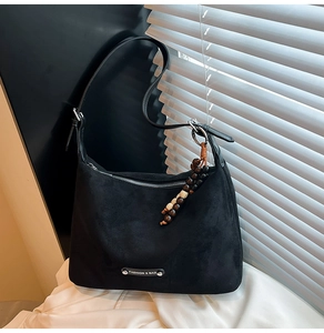 Close-up of black faux suede dumpling bag with metal tag and beaded charm detail